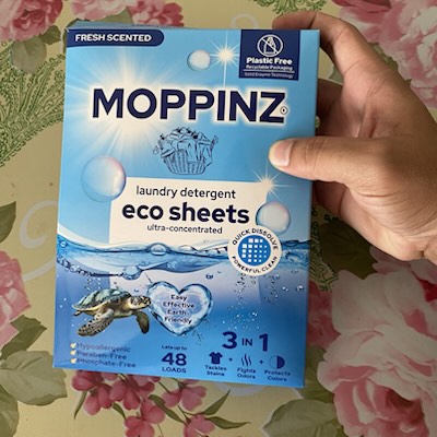 A customer holding the 48-load Moppinz eco laundry sheets box, Fresh Scented, over a floral tablecloth
