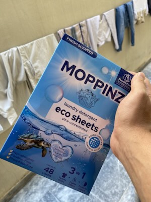 The 48-load Moppinz eco laundry sheets box held in front of shirts and jeans drying on a clothesline