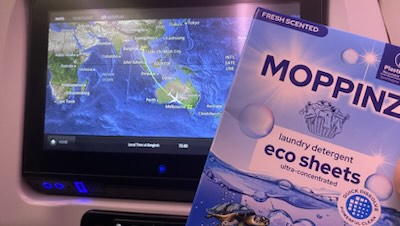 A pack of Moppinz laundry sheets on an aeroplane tray table, in front of the in-flight map screen